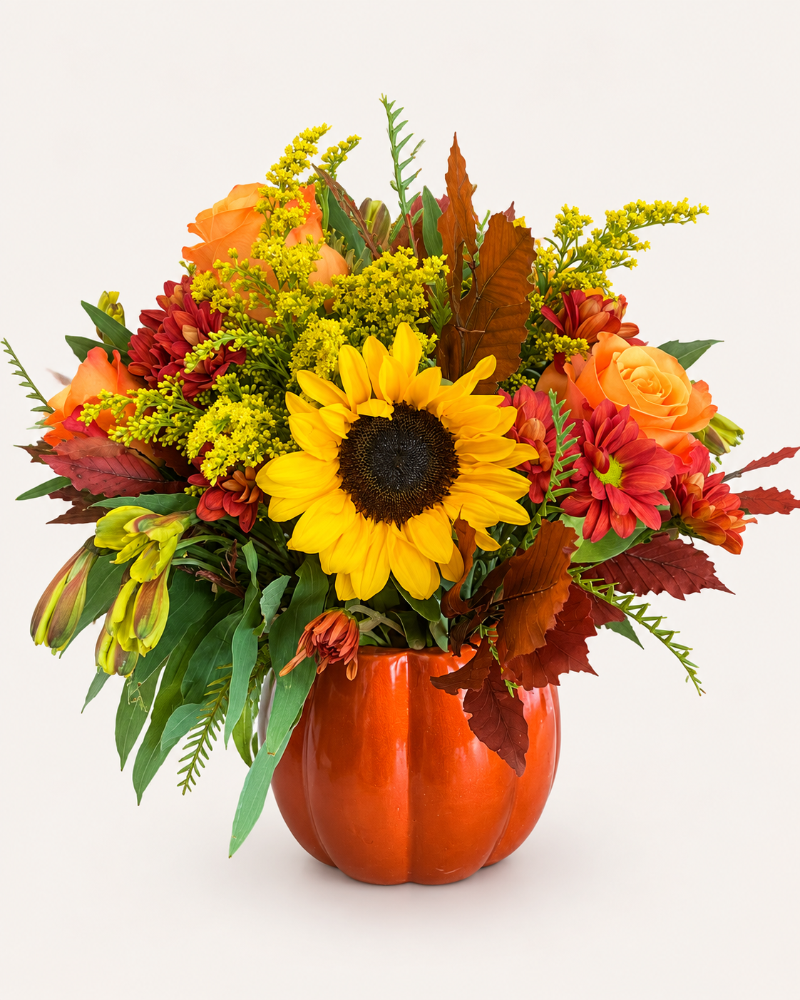 Fall flower arrangement with sunflower, orange roses and autumn blooms in an orange pumpkin vase.